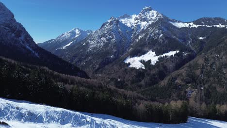 Luftaufnahme-Von-Fußspuren-Im-Schnee-Auf-Einer-Bergstraße-Mit-Kiefernwald-Und-Schneebedeckten-Bergen-Im-Hintergrund-An-Einem-Sonnigen-Tag-Mit-Klarem-Blauen-Himmel-In-Den-österreichischen-Alpen