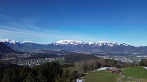 Drone-rise-up-in-sky-fly-above-forest-with-winter-mountain-landscape-and-snowcapped-mountains-on-a-sunny-day-with-blue-sky