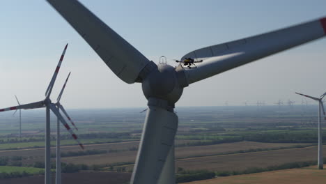 A-drone-in-the-air-surveying-a-working-wind-turbine-to-the-backdrop-of-a-wind-farm-on-flat-farm-land