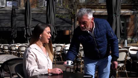 A-gray-haired-waiter-brings-a-coffee-on-a-terrace-in-the-south-of-France-to-a-pretty-young-woman-seated