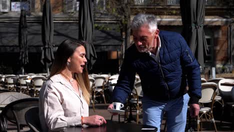 Ein-Grauhaariger-Kellner-Bringt-Einer-Hübschen-Jungen-Frau-Auf-Einer-Terrasse-Im-Süden-Frankreichs-Einen-Kaffee