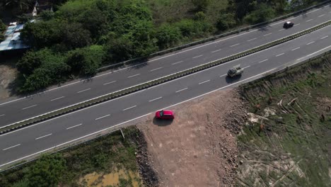 Eine-Dramatische-Luftaufnahme-Eines-Roten-Autos,-Das-Auf-Einer-Autobahn-Am-Meer-Entlang-Fährt