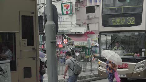 Hong-Kong-pedestrians-walk-with-umbrellas-amongst-public-buses-during-an-overcast-cloudy-day---slow-motion