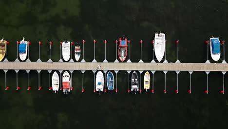 small-harbor-with-many-small-boats,-man-walks-slowly-across-the-jetty,-ocean,-visby,-sweden,-drone