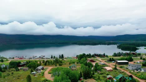 Bird-Flying-over-Beautiful-Grand-Lake-and-Shadow-Mountain-Reservoir-on-a-Cloudy-Summer-Day-with-Cars-Driving-on-Colorado-Highway-Road-Past-Vacation-Homes-Along-the-Overcast-Shoreline