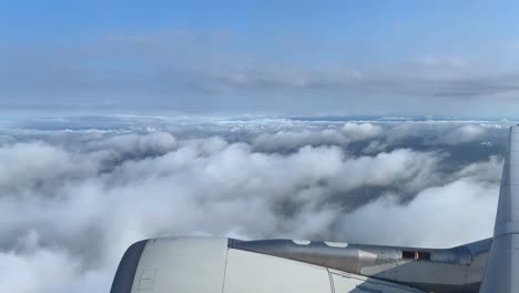 Aerial-view-from-airplane-window-over-clouds-with-visible-jet-engine,-daylight