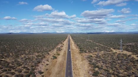 A-straight-road-with-a-white-car-cutting-through-the-vast-desert-of-baja-california-sur,-aerial-view