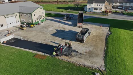 Un-Equipo-Pavimenta-Un-Nuevo-Camino-De-Entrada-Junto-A-Una-Granja-Rural-Mientras-El-Sol-Se-Pone,-Proyectando-Tonos-Cálidos-Sobre-La-Tranquila-Escena.