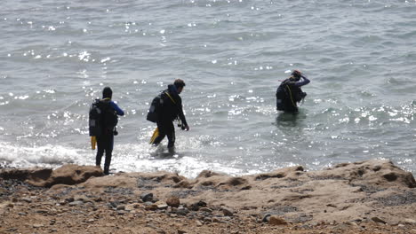 Taucher-In-Eleganter-Taucherausrüstung-Brechen-Von-Einem-Felsigen-Strand-Auf-Und-Trotzen-Den-Glitzernden-Wellen-Für-Ein-Aufregendes-Meeresabenteuer