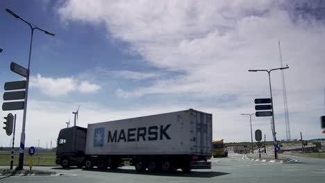 Trucks-at-roundabout-with-clear-skies,-wind-turbines-in-background,-industrial-setting