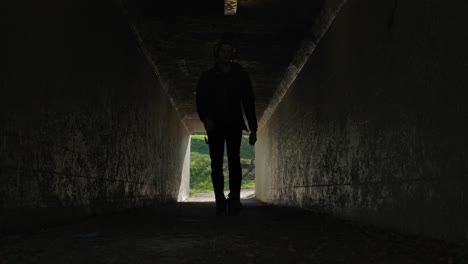 Silhouetted-figure-walks-through-tunnel,-bright-daylight-visible-outside,-conveying-hope,-mystery