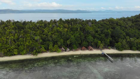 Vollkommen-Klares-Wasser-Mit-Türkisfarbenem-Meeresboden-Vor-Dem-Inselparadies-Kri-In-Raja-Ampat,-Indonesien-Mit-Palmen-Und-Ferienhütten,-Luftaufnahme-Von-Oben