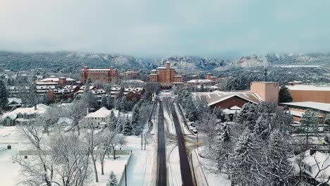 Drone-reverse-dolly-along-straight-snow-covered-road-away-from-hotel-passing-neighborhood-in-Colorado