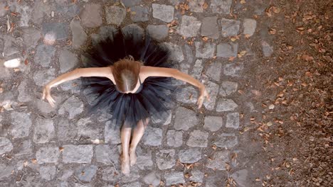 Junge-Balletttänzerin-Im-Schwarzen-Tutu-Sitzt-Im-Freien-Und-Bewegt-Ihre-Arme