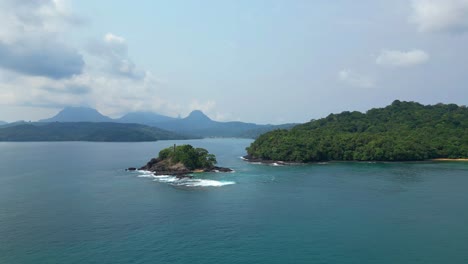 Aerial-tracking-shot-low-in-front-of-Prince-Island-coast-and-a-small-islet,Ilha-do-Principe,Africa