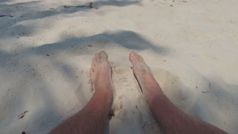 POV-shot-of-the-male-legs-digging-in-the-clear-white-sand-on-the-beach