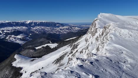 Picos-Nevados-De-Piatra-Craiului-Vistos-Desde-Las-Montañas-De-Bucegi-Bajo-Un-Cielo-Azul-Claro,-Vista-Aérea