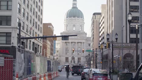 Vea-La-Carretera-En-Indianápolis,-Indiana,-Del-Edificio-Del-Capitolio-Del-Estado-De-Indiana-Con-Tráfico-De-Vehículos-Y-Un-Ciclista-Que-Pasa-Con-Video-Estable