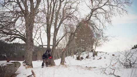 Man-Cutting-Logs-With-Chainsaw-In-The-Forest-During-Winter---Wide-Shot