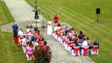 Una-Ceremonia-De-Boda-Secular-En-Un-Gran-Jardín,-Código-De-Vestimenta-Rojo-Y-Blanco,-La-Novia-Espera-A-Su-Esposa