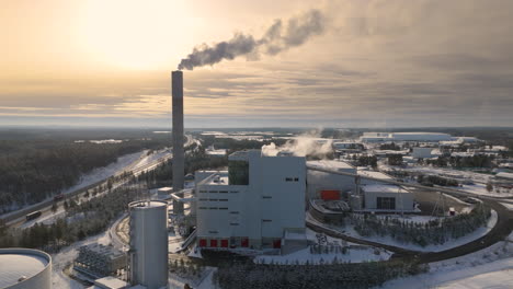Jonkoping-Energi-power-station-emitting-gases-against-sunset-sky,-winter-aerial