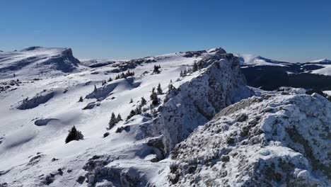 Snow-covered-Strungile-Mari-Peak-in-the-Bucegi-Mountains-under-a-clear-blue-sky,-aerial-view