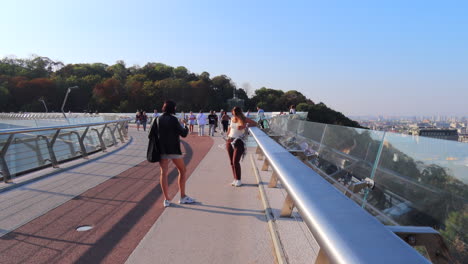 People-walking-and-taking-photos-on-the-famous-Glass-Bridge-in-Kyiv-city-center-Ukraine,-sunny-weather-and-blue-sky,-bridge-with-glass-floor-panels,-4K-shot