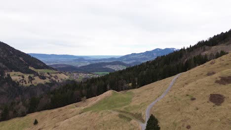 Tilt-up-aerial-drone-shot-of-mountain-road-with-wide-view-over-town-in-Vorarlberg-Austria