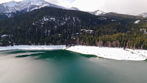 Hermosa-Vista-Aérea-Del-Lago-Kachess-Con-Bancos-De-Nieve-Y-árboles-De-Hoja-Perenne-Con-Montañas-Cubiertas-De-Nieve-En-El-Estado-De-Washington