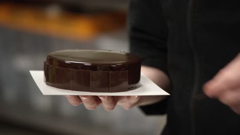 Close-up-of-a-person-decorating-a-shiny-chocolate-cake-on-a-plate,-in-a-kitchen