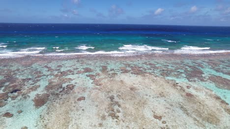 Clear-turquoise-waters-and-gentle-waves-over-a-coral-reef-at-Los-Roques,-aerial-forward-movement