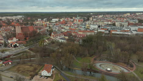 An-aerial-view-of-the-historic-city-center-of-Olsztyn,-Poland,-with-its-colorful-buildings,-prominent-red-roofs,-and-the-castle,-all-interwoven-with-the-city's-green-park-spaces-and-a-winding-river