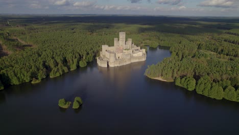 Aerial-orbit-shot-of-the-beautiful-Castle-of-Stobnica,-Poland---a-big-tourist-attraction-built-on-an-artificial-island-on-a-lake-in-the-middle-of-an-unhabituated-forest
