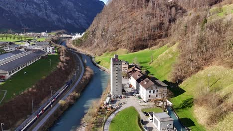 Aerial-approaching-shot-of-tower-and-rolling-mill-factory-beside-river-and-riding-train