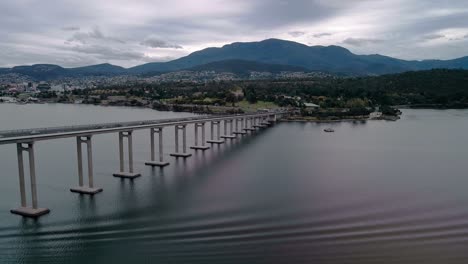 Backward-shot-of-bridge-standing-still-on-a-river-with-range-of-mountains-at-background