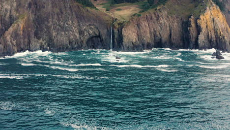 Wide-aerial-pullout-over-Pacific-Ocean,-away-from-rocky-cliff-of-Oregon-coast