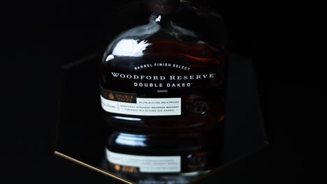 Wunderschöne-Reflexionen-Einer-Flasche-Woodford-Reserve-Kentucky-Straight-Bourbon-Whiskey-Aus-Doppelter-Eiche-Auf-Einem-Spiegel-Mit-Einem-Dunkelschwarzen-Hintergrund,-Der-Das-Produkt-Hervorstechen-Lässt