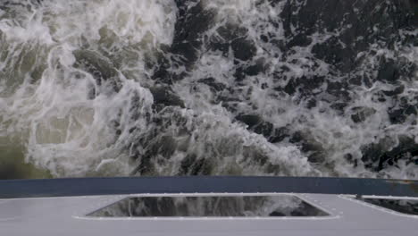 Slow-motion-shot-down-the-hull-of-a-boat-towards-the-water-going-past-and-leaving-wake---Milford-Sound-,-New-Zealand