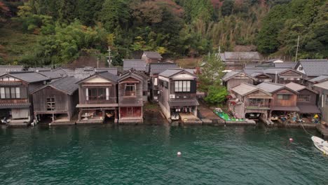 Drones-En-Cámara-Lenta-Vuelan-Sobre-Los-Cobertizos-Para-Botes-Ine-cho,-Japón-Kyotango-Pueblo-Mar-Azul-Panorámica-Aérea-De-Casas-Tradicionales-De-Madera