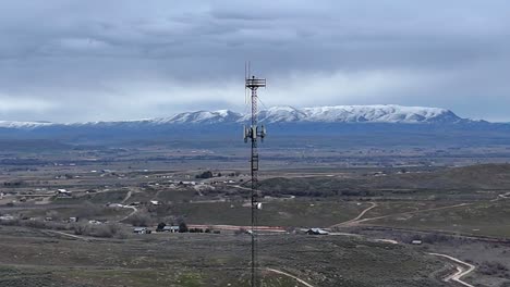 Drone-flying-orbit-around-very-tall-cell-phone-tower-in-late-overcast-winter-evening-over-barren-desert-landscape