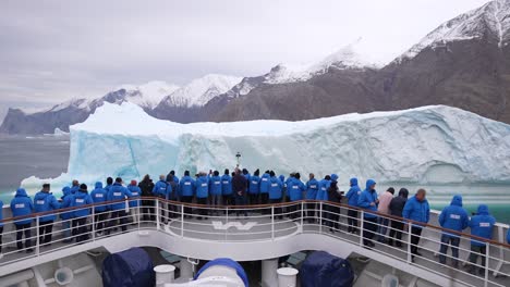 Cruise-Ship-Passengers-on-Front-Deck-in-Front-of-Massive-Iceberg-in-Fjord,-Slow-Motion