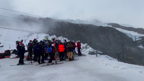 Saas-Fee-alpine-ski-racing-racer-morning-crowd-of-people-skier-skiing-up-training-gates-glacier-waiting-for-bar-ski-lift-Saastal-Swiss-alp-Switzerland-cinematic-follow-left-up-mountain-peak-pan-motion