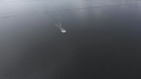 Aerial-drone-view-of-a-small-boat-moving-in-the-middle-of-the-water-where-a-much-larger-lake-is-located-with-waves-behind-it