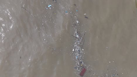 Low-altitude-top-down-drone-shot-of-polluted-water-filled-with-floating-trash-and-muddy-river-runoff-mixing-with-turqouise-tropical-water-of-Bali-Indonesia