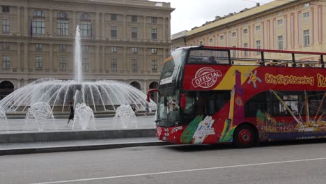 Panning-clip-of-a-red-tour-bus-parked-in-piazza-in-Italy,-in-front-of-famous-water-fountains-and-beautiful-traditional-buildings