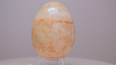 Orange-and-cream-Marble-egg-rotating-slowly-on-a-turntable-in-front-of-a-white-background