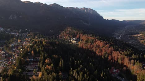 Autumnal-aerial-view-of-Sinaia-and-Peles-Castle-in-Romania,-surrounded-by-colorful-forest