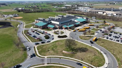 Drohnenflug-über-Amerikanische-Schule-Mit-Parkenden-Gelben-Bussen-Und-Verkehr-Im-Kreisverkehr