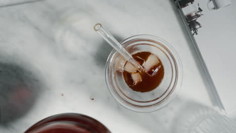 Top-view-iced-coffee-in-glass-with-stirrer-on-marble