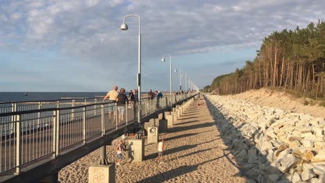 Promenada-Przyjazni-bridge-in-Mielno,-Poland-at-shore-of-Baltic-Sea-at-sunset-with-people-walking